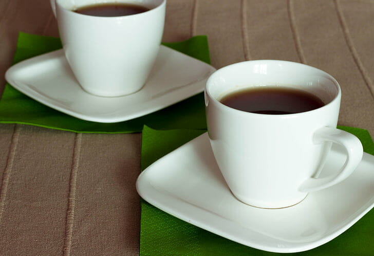 Two handled cups on saucers. They have brown liquid in them.