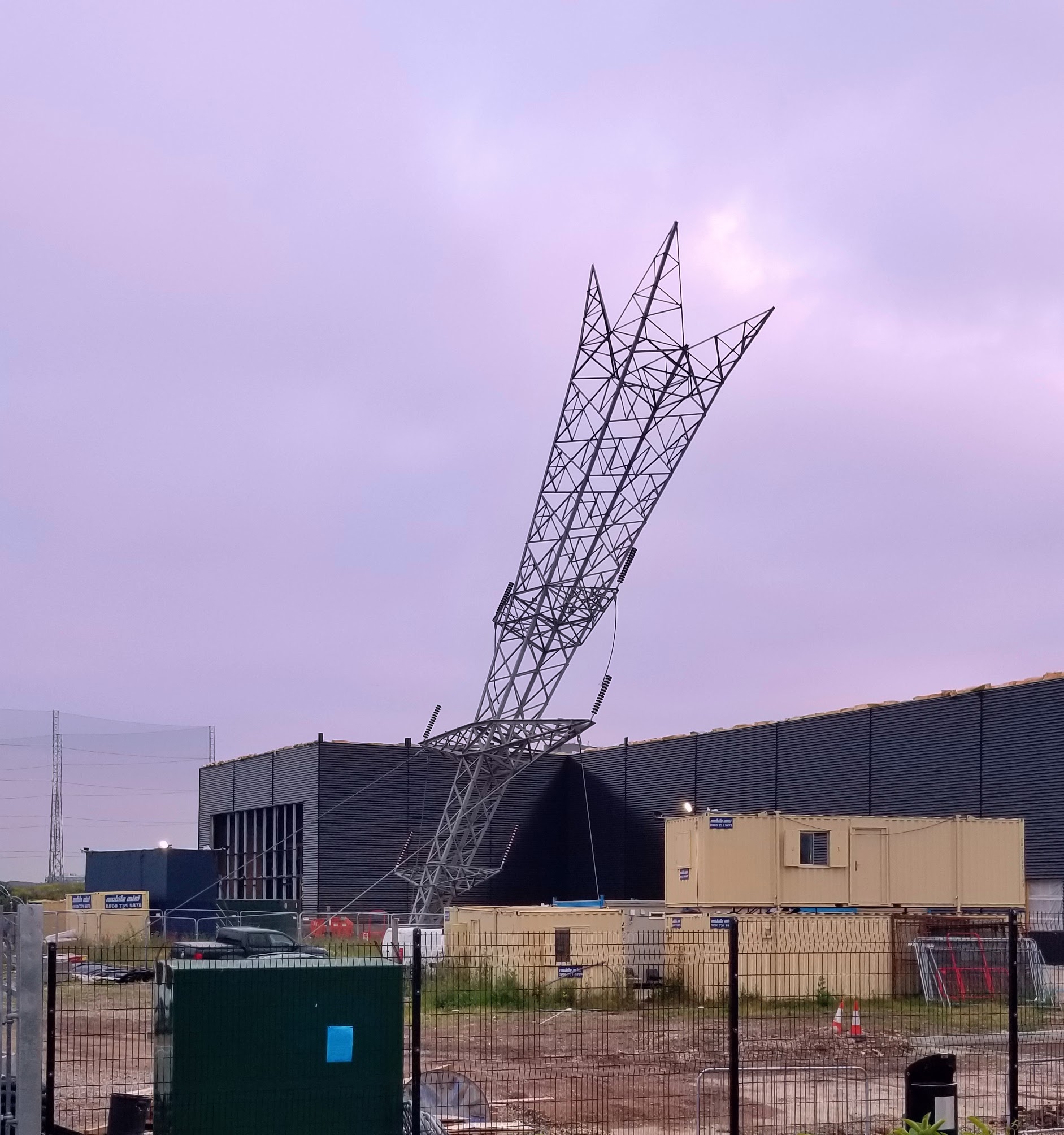 An art piece where an electrical pylon is set on its tip in an industrial park, as if it were a lawn dart of the gods