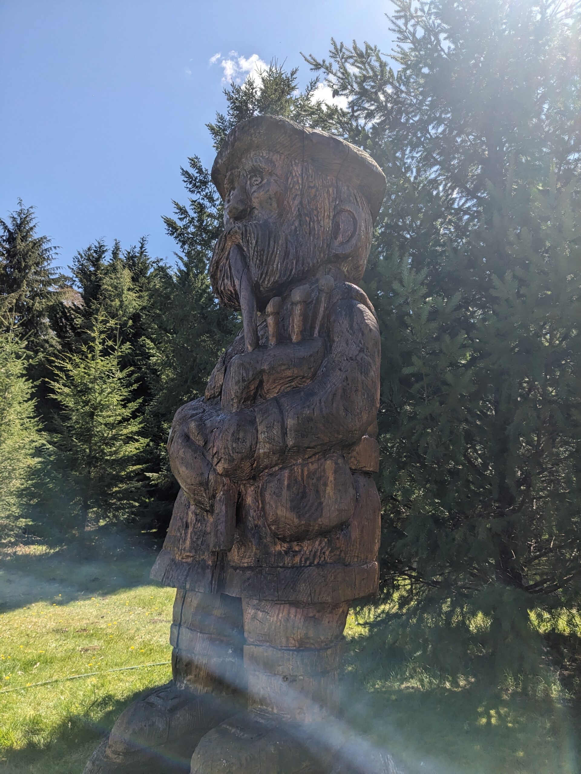 A chainsaw carving of a Scottish piper, wearing a tam, kilt, sporran, hose, and buckled shoes. And a beard. All carefully rendered in a log.